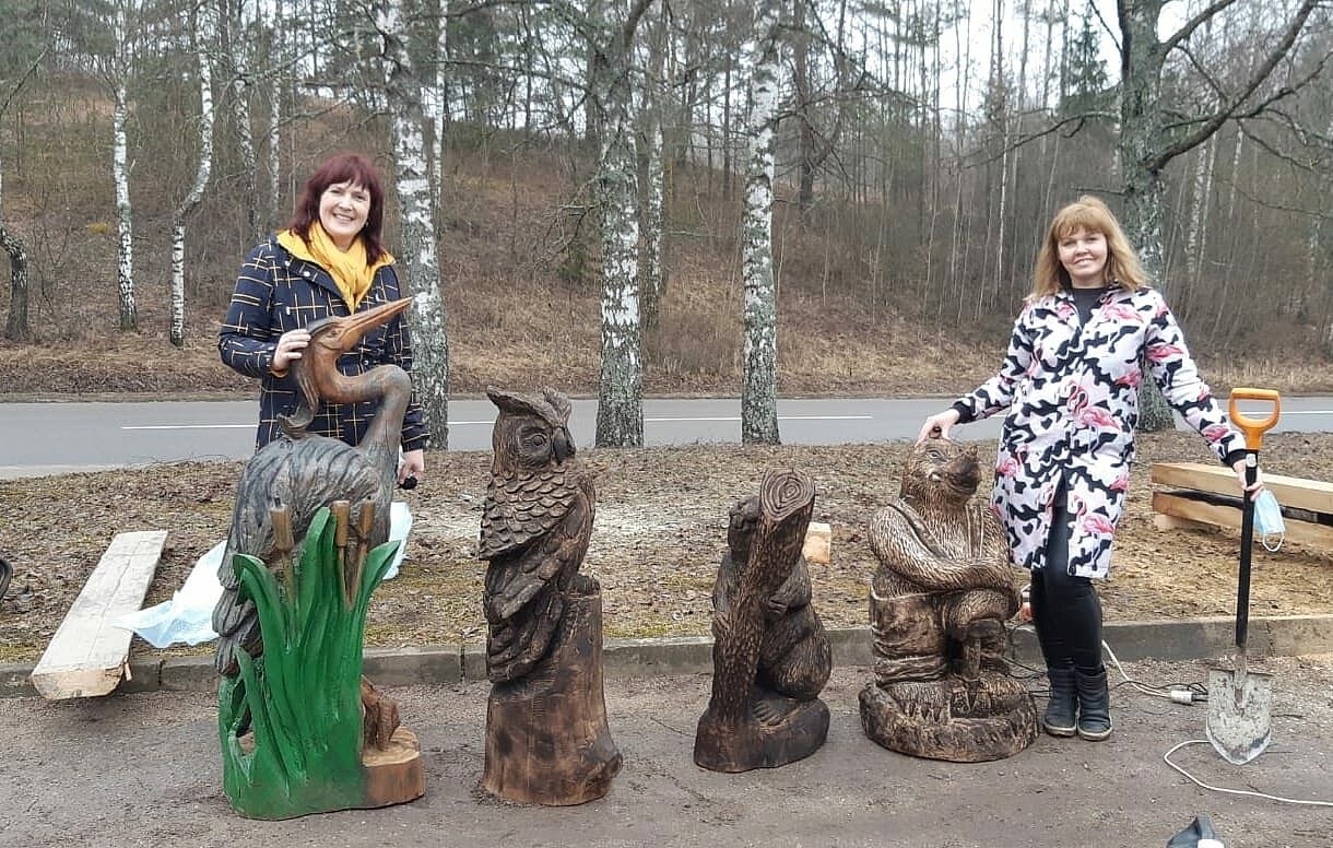 Divi cilvēki pie stārķa, pūces, bebra un kurmja koka statujām