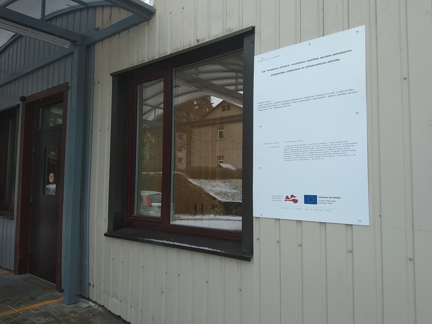 Piestiprināta projekta plāksnīte pie slimnīcas sienas