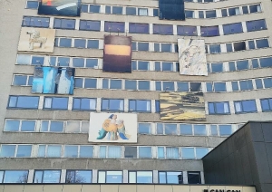 Daudzstāvu ēka ar vairākām lielizmēra gleznām piekārtām pie fasādes