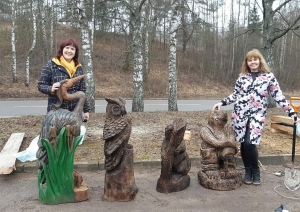 Divi cilvēki pie stārķa, pūces, bebra un kurmja koka statujām