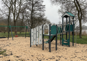 Bērnu rotaļu laukums pie ezera – kāpelēšanas konstrukcija un šūpoles smilšu laukumā