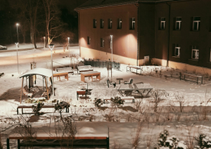 Sniegots pagalms pie ēkas ar soliem, galdiem un dekoratīviem krūmiem