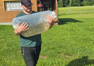 Vīrietis nes lielu caurspīdīgu maisu ar zivju mazuļiem pie ezera
