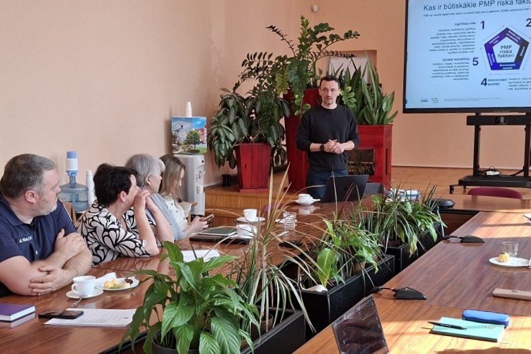 Prezentētājs runā pie galda ar auditoriju