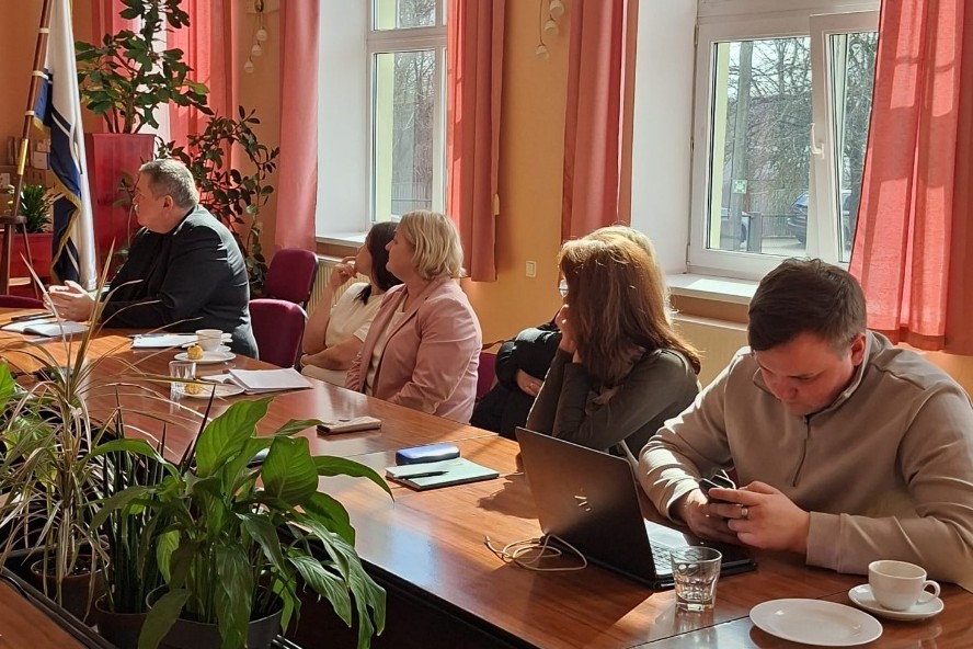 Cilvēki sēž pie galda, klausās prezentāciju