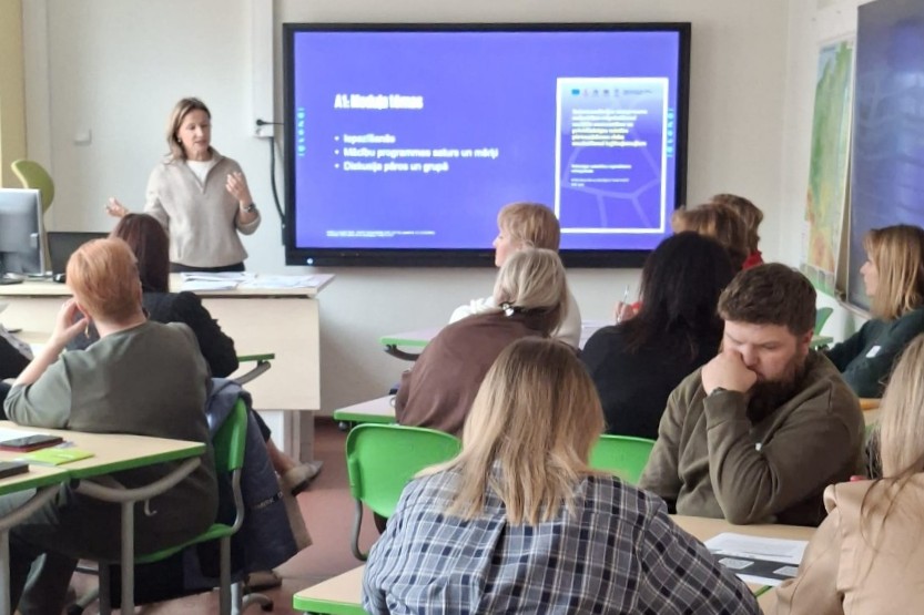 Apmācību klase ar prezentāciju uz ekrāna, dalībnieki strādā un klausās