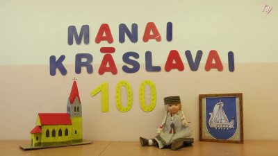 No kartona pa burtam izgriezts un pie sienas piestiprināts uzraksts "MANAI KRĀSLAVAI 100". Uz galda stāv rāmītis ar Krāslavas ģērboni, lelle ģērbta tautastērpā un no kartona veidota Krāslavas luterāņu baznīca