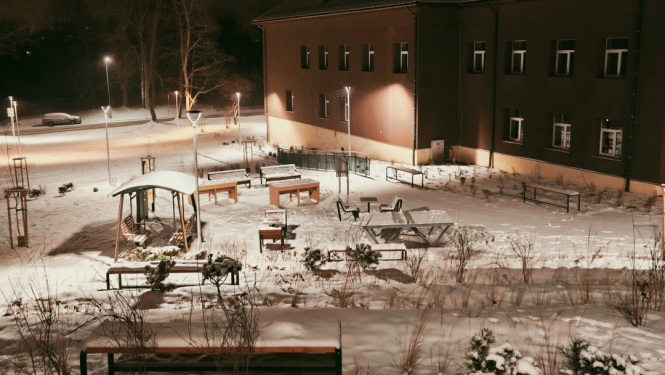 Sniegots pagalms pie ēkas ar soliem, galdiem un dekoratīviem krūmiem