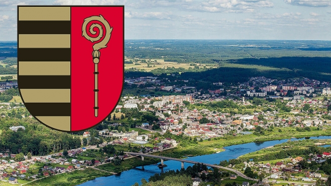 Foto ar skatu uz Krāslavu no augstuma un Krāslavas novada ģērbonis attēla kreisajā, augšējā stūrī