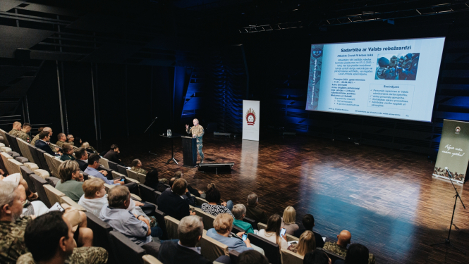 Cilvēki sēž zālē un klausās Valsts robežsardzes prezentāciju