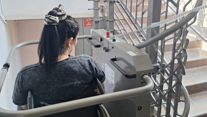 Persona ratiņkrēslā izmanto kāpņu pacēlāju ēkas iekšpusē.