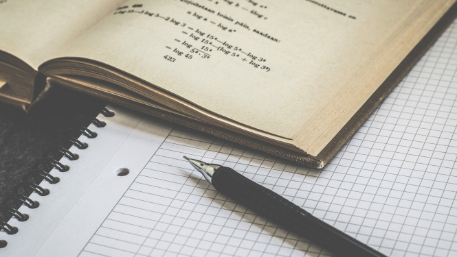 Uz galda atvērta matemātikas grāmata, rūtiņu klade un pildspalva