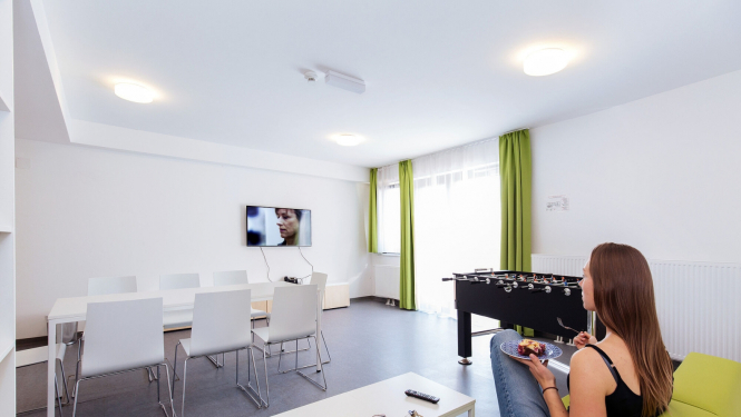 Meitene sēž uz dīvāna un skatās televizoru plašā, gaišā telpā