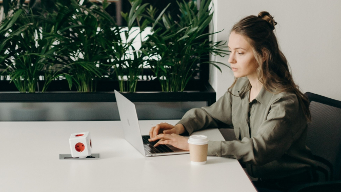 Sieviete sēž pie galda un izmanto portatīvo datoru