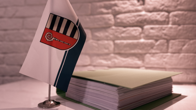 Uz galda stāv karodziņš ar Krāslavas novada ģērboni un dokumentu mape