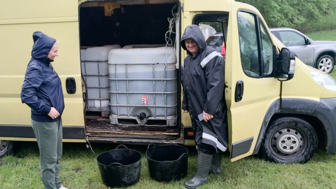 Cilvēki pie mašīnas, kurā iekrauti zivju mazuļi