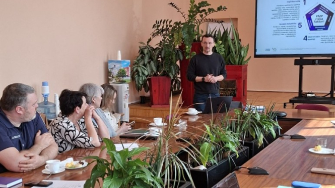 Prezentētājs runā pie galda ar auditoriju
