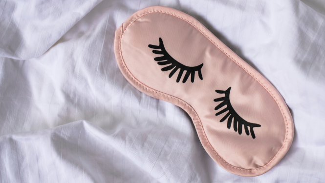 Persiku krāsas miega maska guļ uz baltas segas