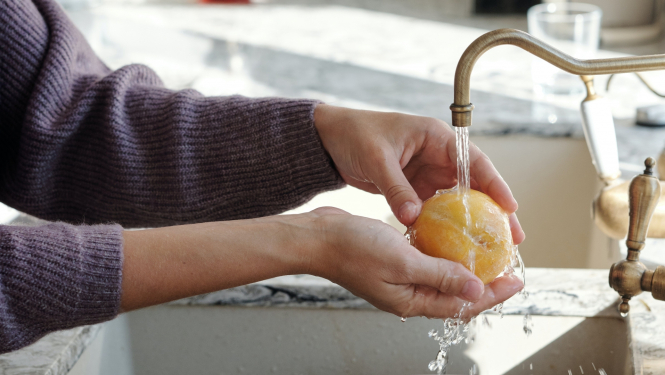 Sieviete zem tekoša krāna ūdens mazgā persiku