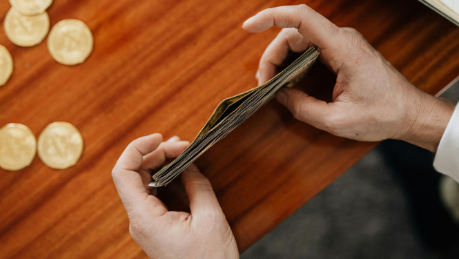 Seniors, sēžot pie galda, tur rokās banknotes.