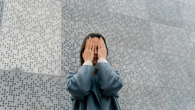 Sieviete aizklāj seju ar rokām, stāvot priekšā punktainai sienai
