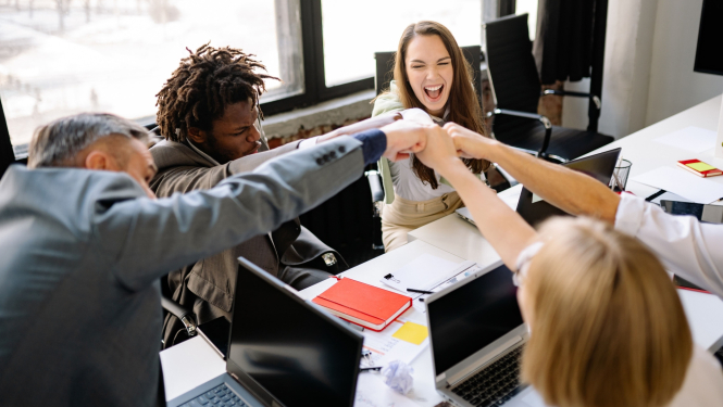 Cilvēki, sēžot pie galda, izstiepj savas rokas lai pieskartos viens otram ar dūrēm