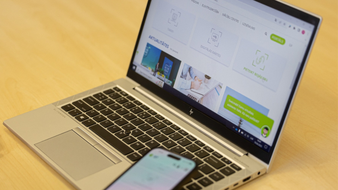 Uz galda stāv klēpjdators, kurā ir atvērta "Sadales tīkla" tīmekļvietne