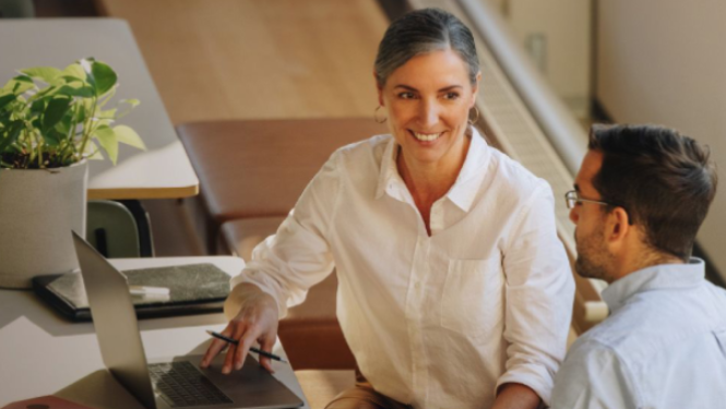 Divi cilvēki sēž pie galda ar klēpjdatoru.