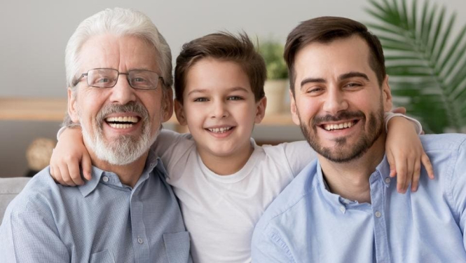 Dēls, tēvs un vectēvs sēž uz dīvāna, apskāvušies