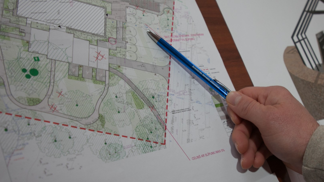 Cilvēka roka, kur ar pildspalvu norāda uz punktu plānojumā