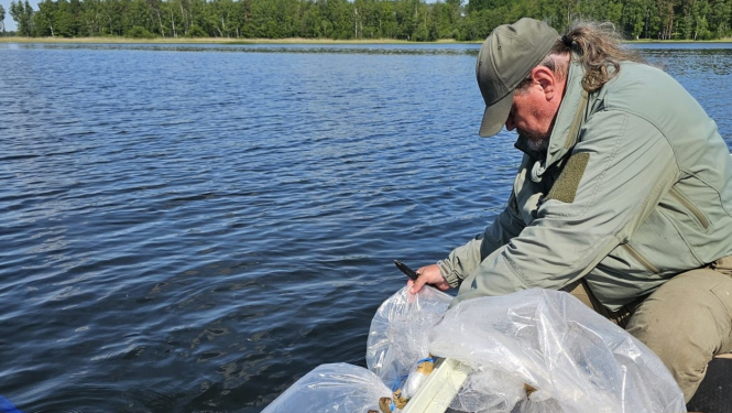 Cilvēks, sēžot laivā, palaiž zivju mazuļus ezerā