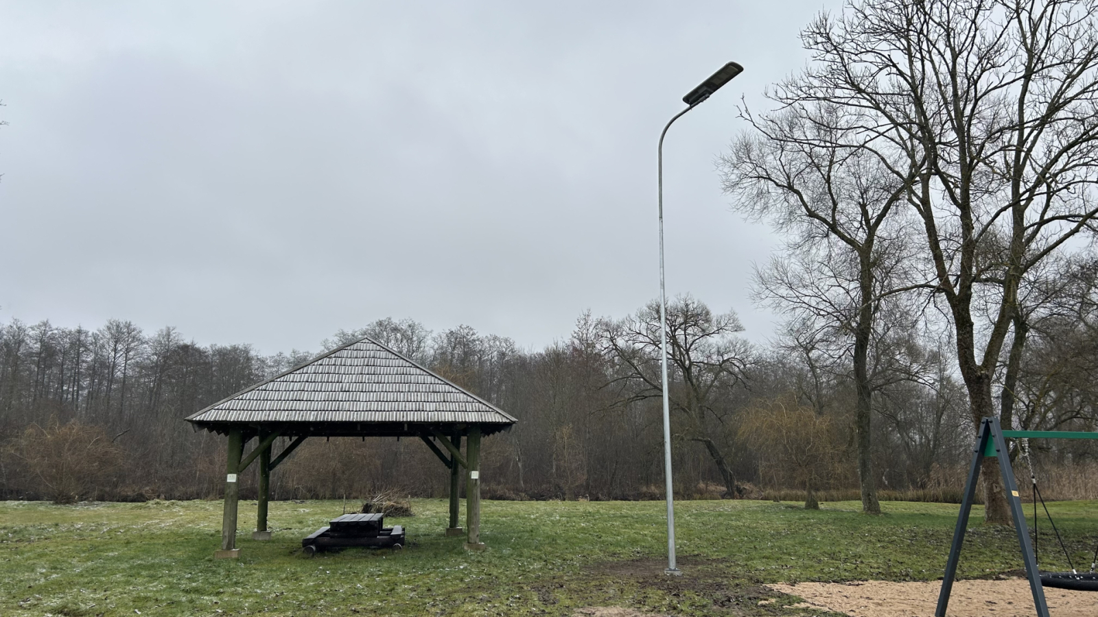 Lapene un laterna parkā – koka lapene zālājā pie kokiem un laterna blakus