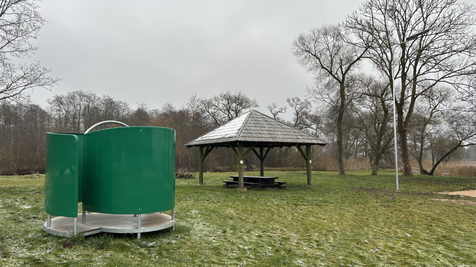 Āra pārģērbšanās kabīne un lapene – zaļa pārģērbšanās kabīne blakus koka lapenei zālājā