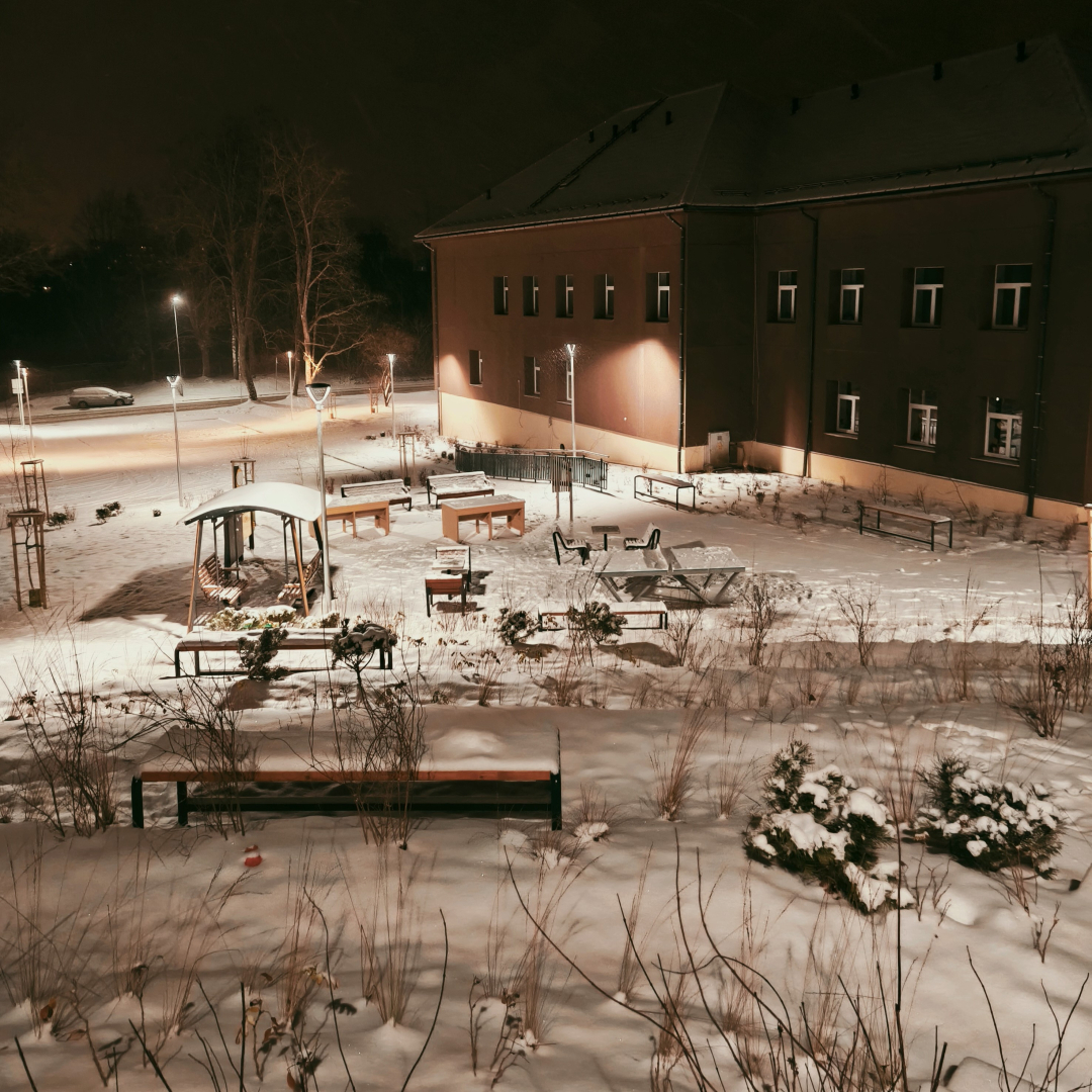 Sniegots pagalms pie ēkas ar soliem, galdiem un dekoratīviem krūmiem