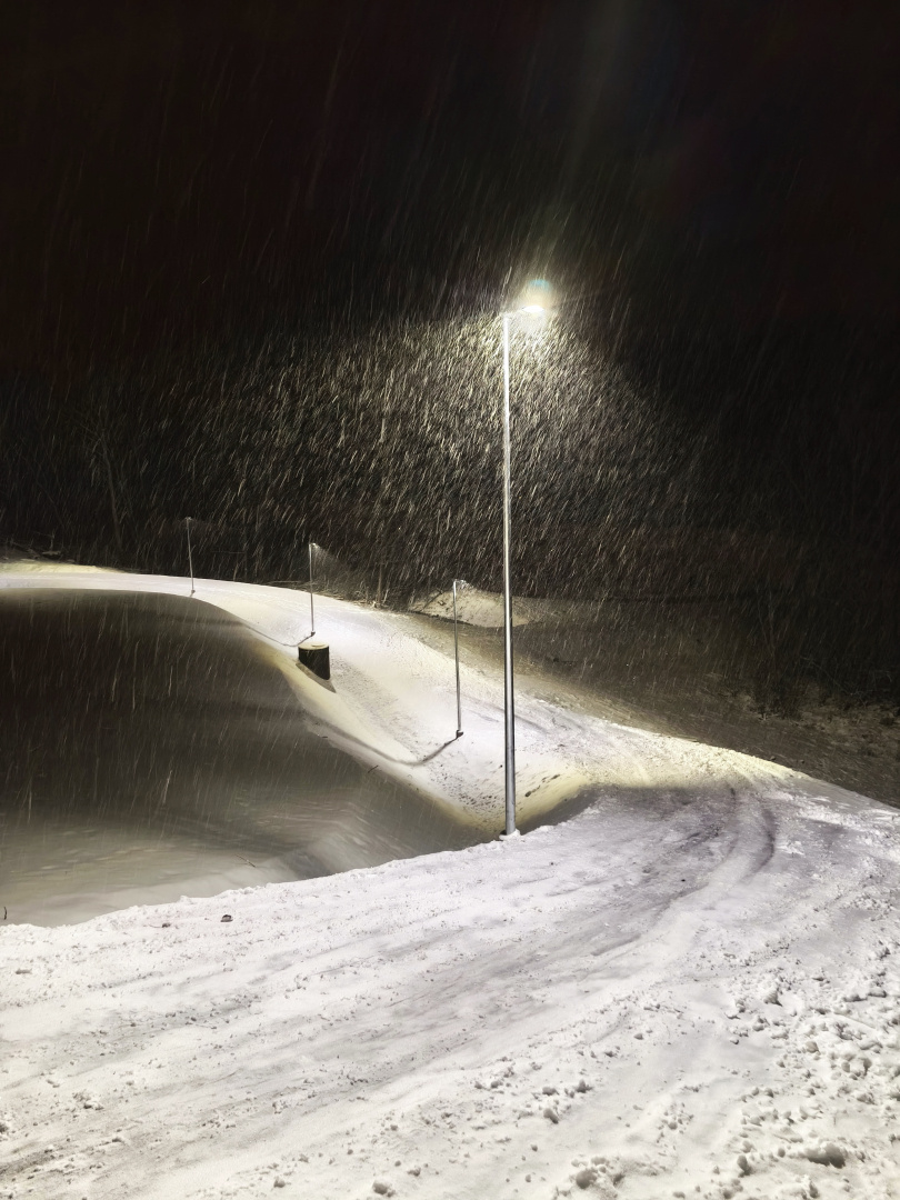 Stāvs, sniegots ceļš stadionā, apgaismots ar laternu stiprā sniegputenī