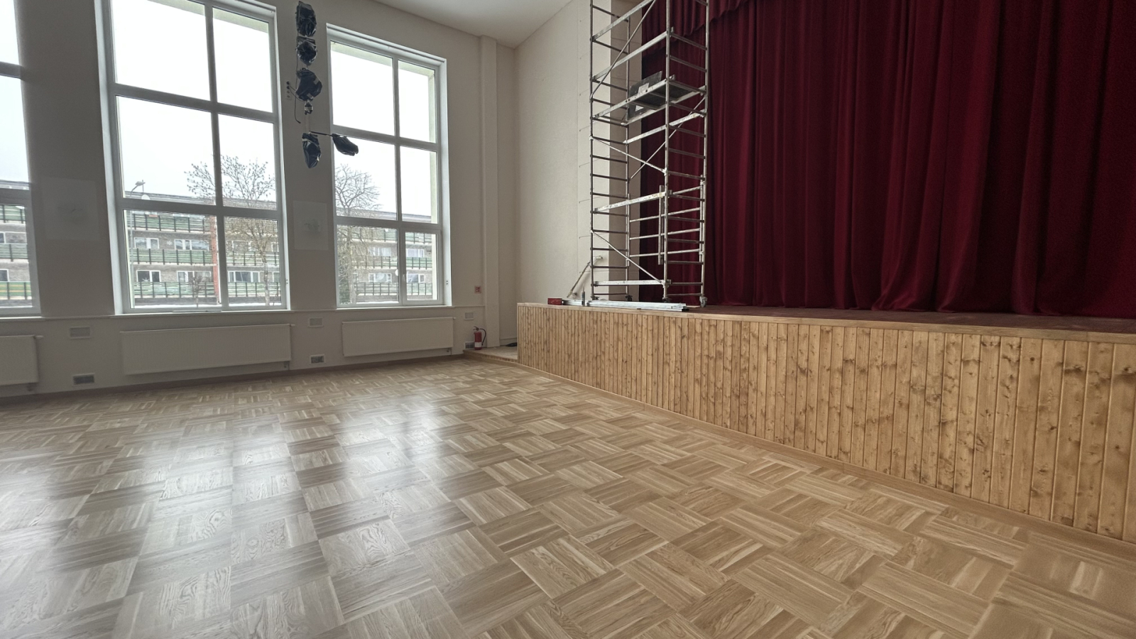 Zāle ar skatuvi, sarkaniem aizkariem un sastatnēm.