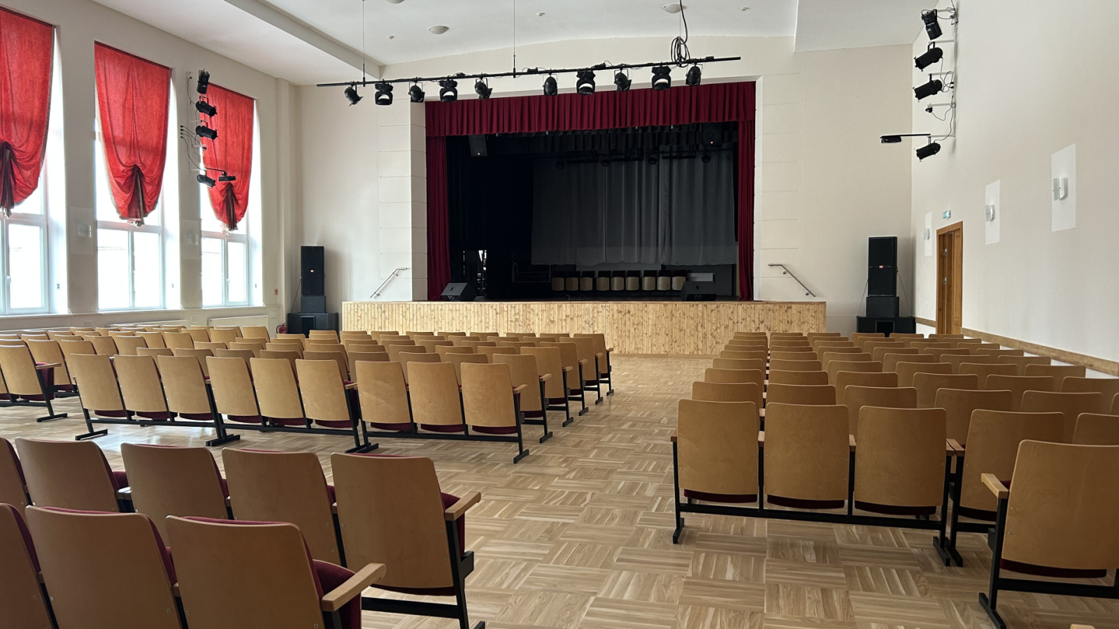 Zāle ar krēsliem, skats uz skatuvi ar aizkariem.
