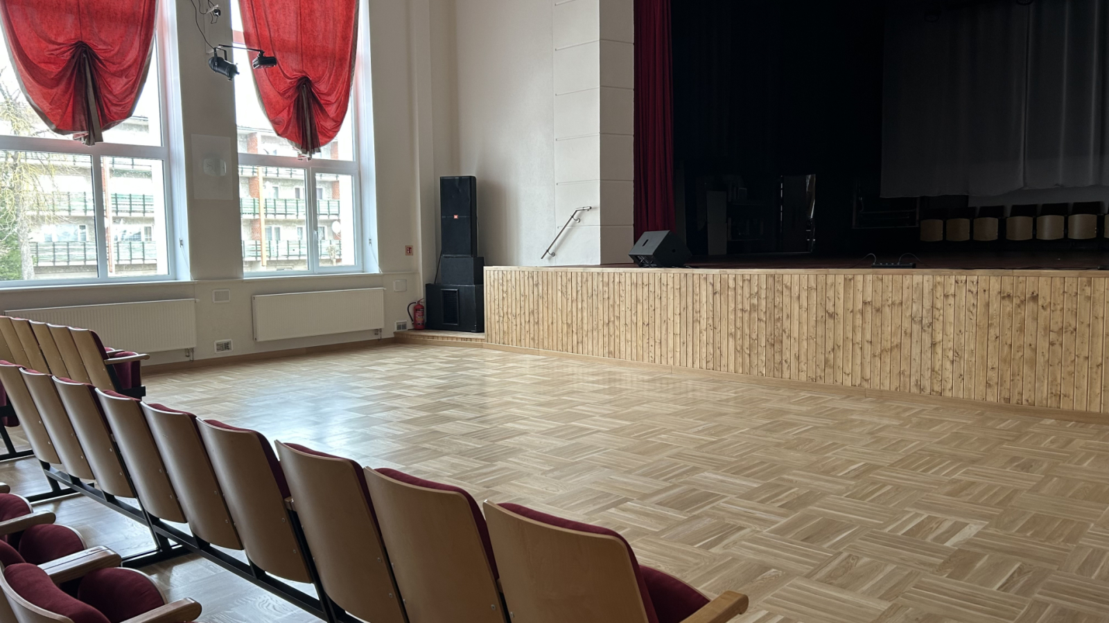 Zāle ar krēsliem un skatuves malu sānskatā.