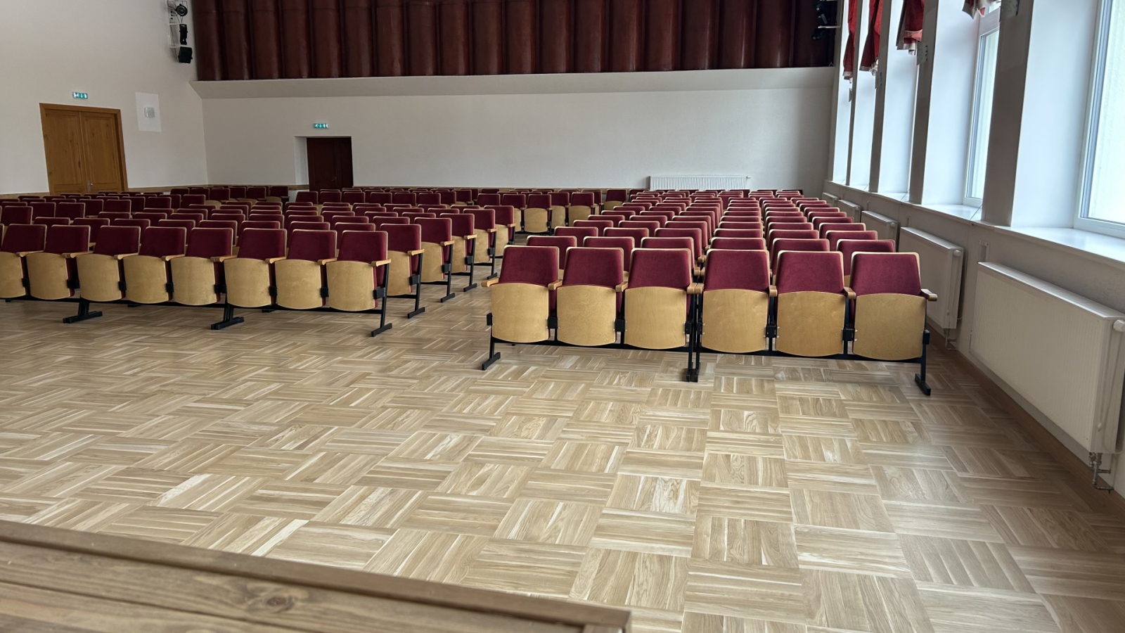 Zāle ar krēsliem un logiem gar sienu.