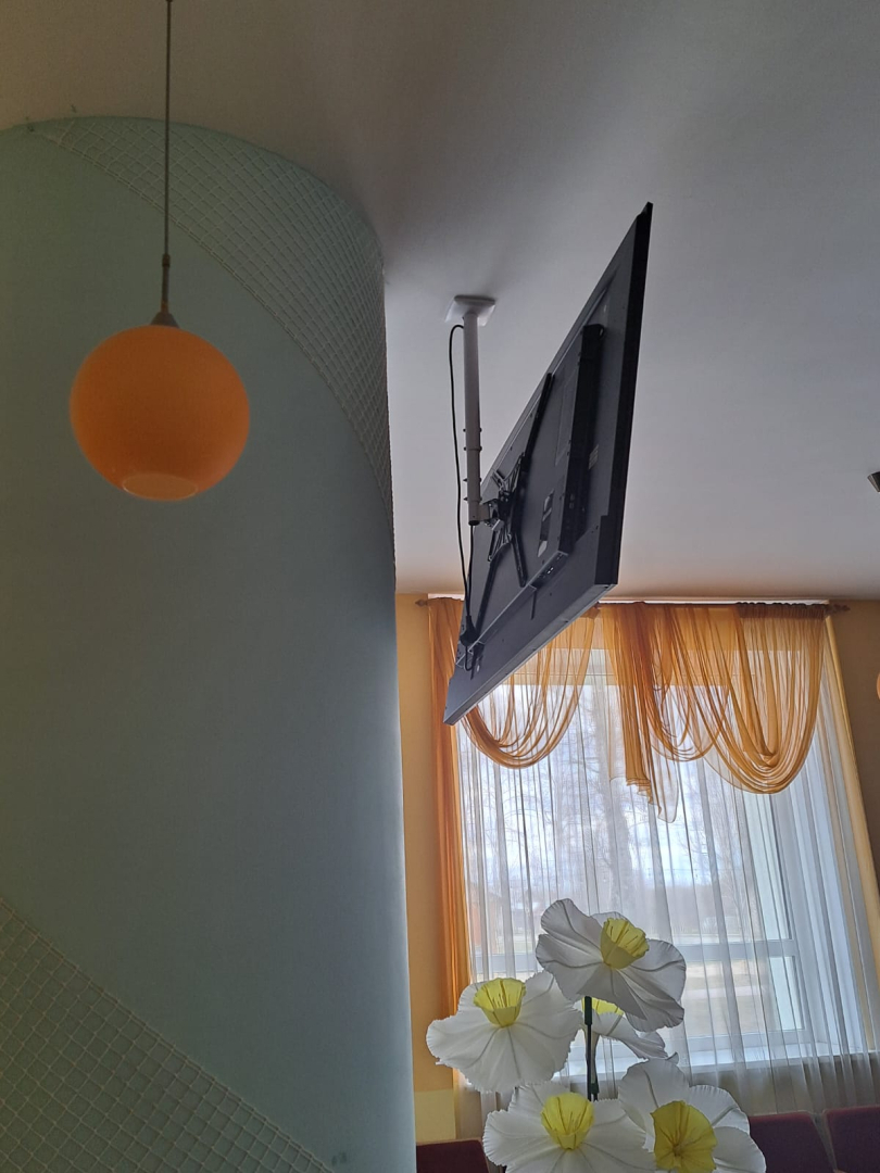 Telpa ar kolonnām, lampām un piekārtu ekrānu.