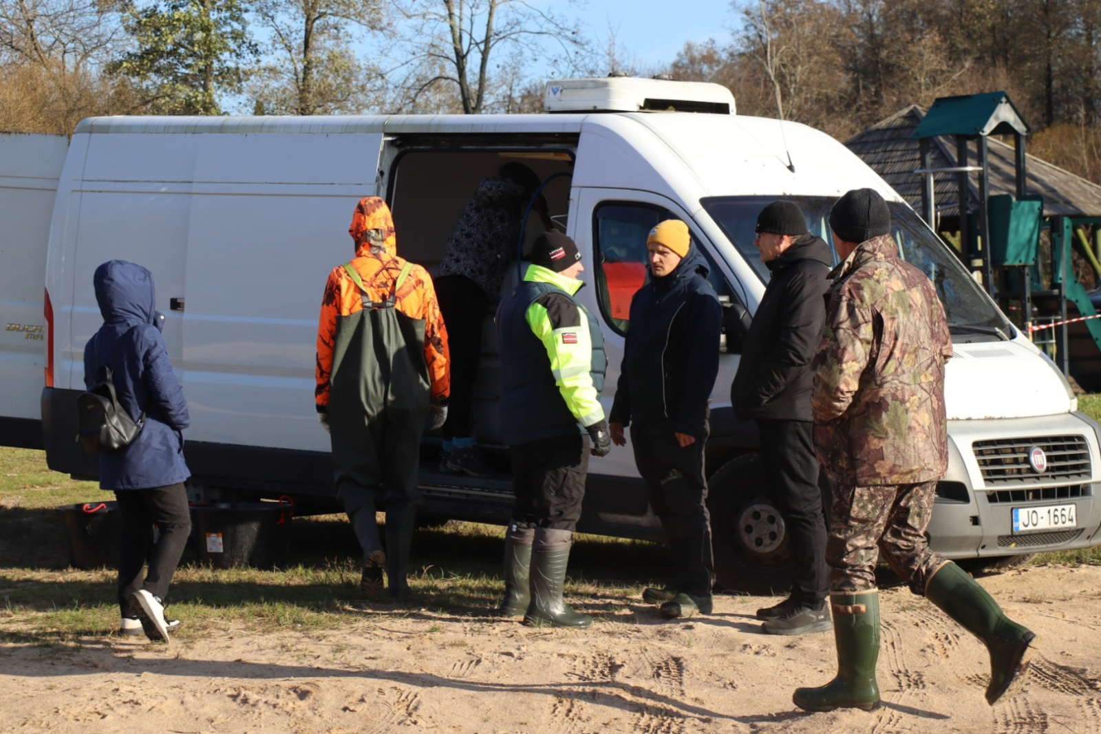 Cilvēki stāv pie atvērta, balta furgona