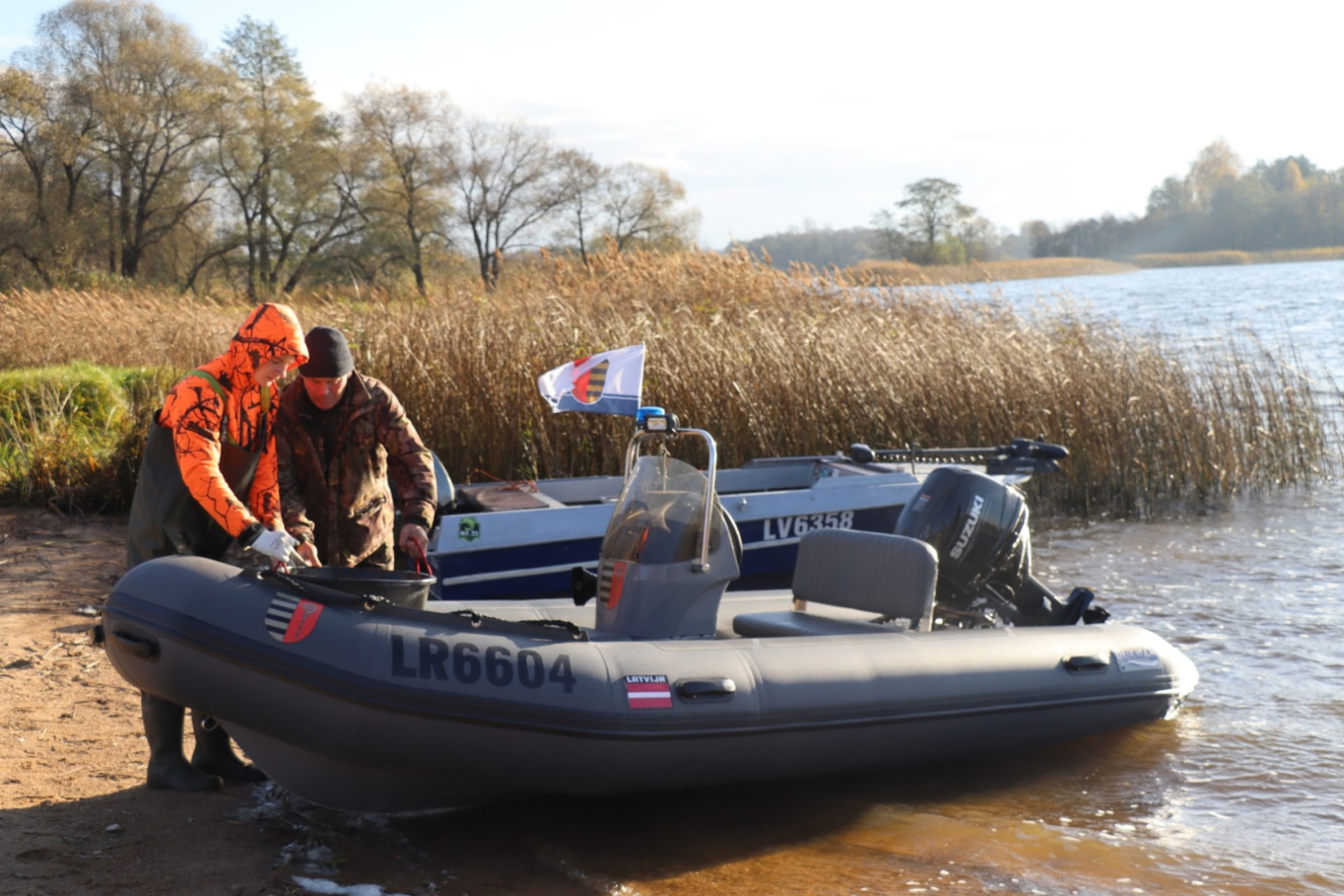 Divi cilvēki pie krasta gatavo gumijas laivu baucienam