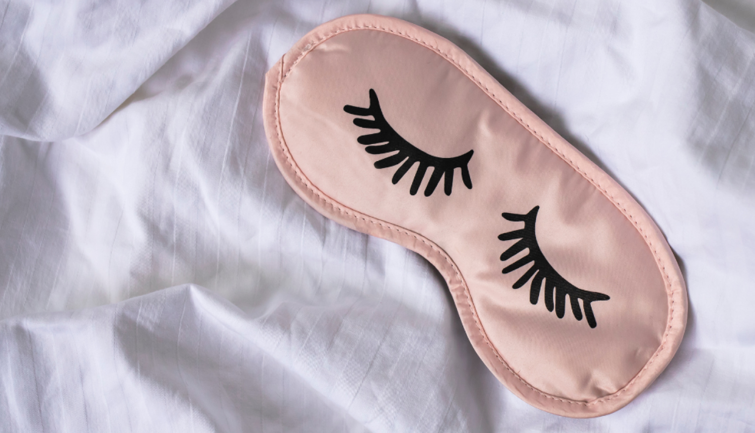 Persiku krāsas miega maska guļ uz baltas segas