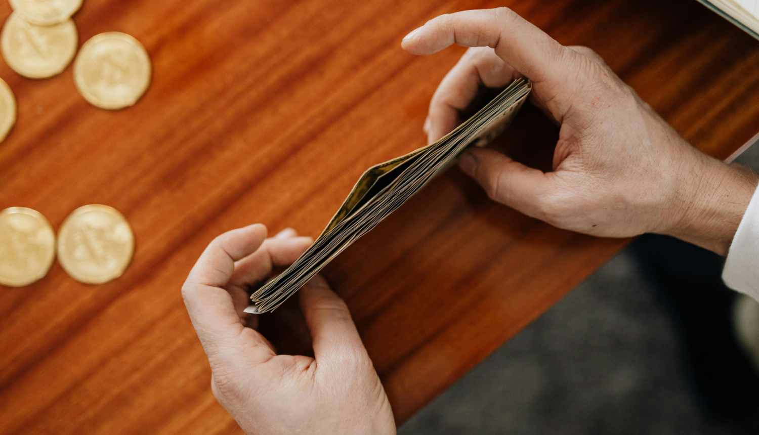 Seniors, sēžot pie galda, tur rokās banknotes.