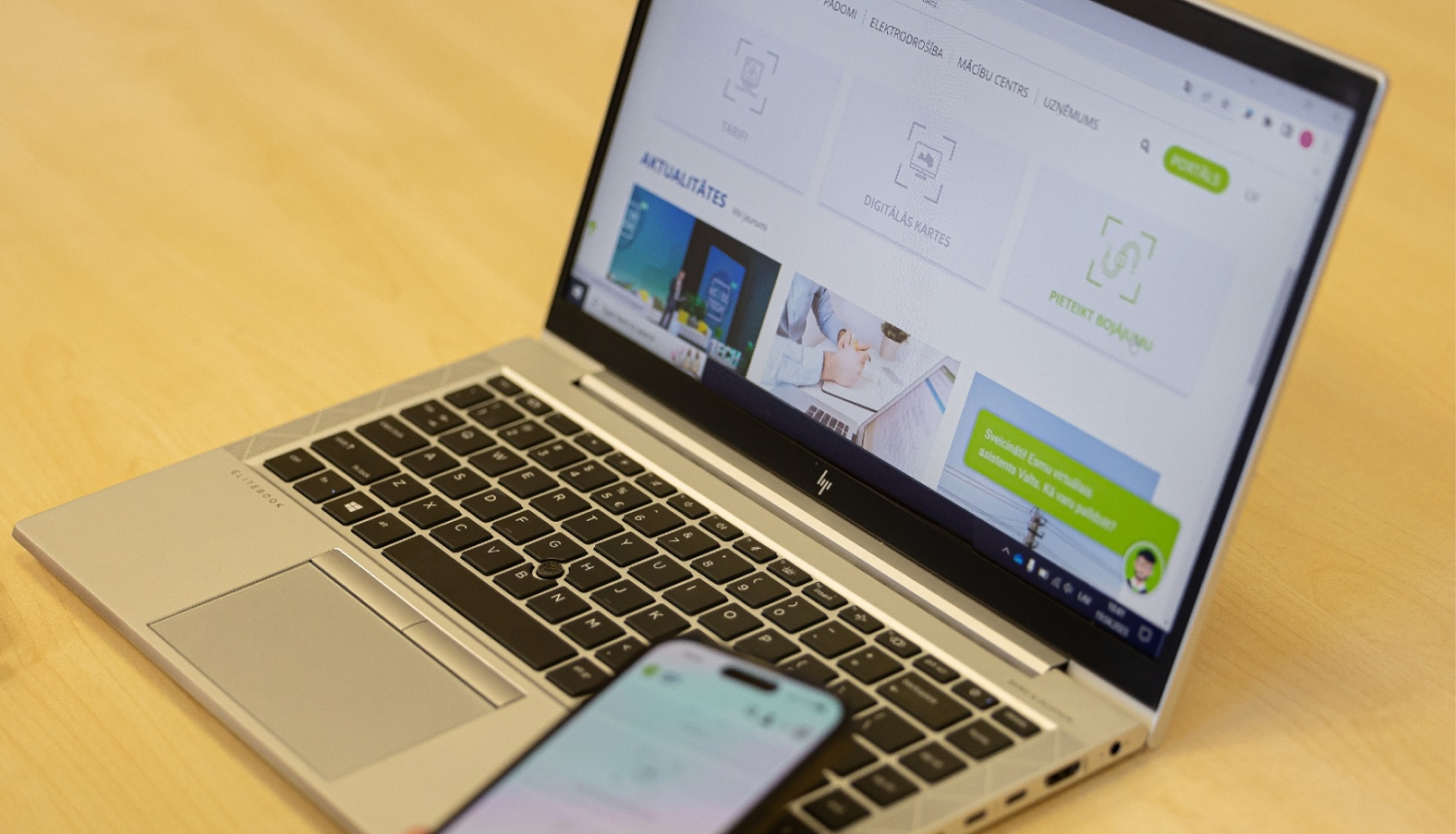 Uz galda stāv klēpjdators, kurā ir atvērta "Sadales tīkla" tīmekļvietne