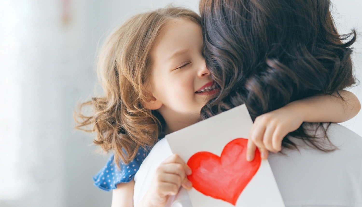 Meitene, apskāvusi mammu, tur rokās kartiņu ar uzzīmētu sirdi