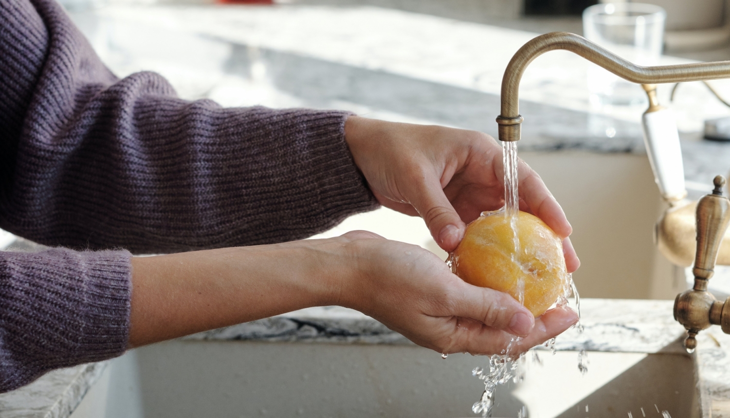 Sieviete zem tekoša krāna ūdens mazgā persiku