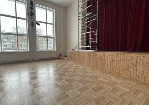 Zāle ar skatuvi, sarkaniem aizkariem un sastatnēm.