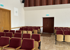 Krēslu rindas zālē un durvis aizmugurē.