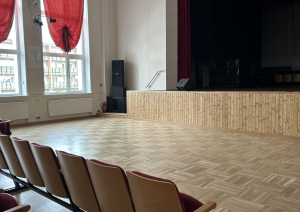 Zāle ar krēsliem un skatuves malu sānskatā.